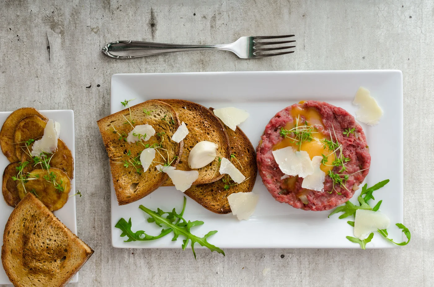 Beef tartar, toast bread with garlic, sprinkled with parmesan shavings and microgreens
