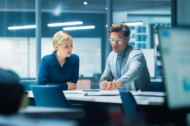 Zwei Geschäftsleute arbeiten gemeinsam an Dokumenten und Strategien in einer modernen Büroumgebung – veranschaulicht Teamarbeit, Planung und effektive Kommunikation.