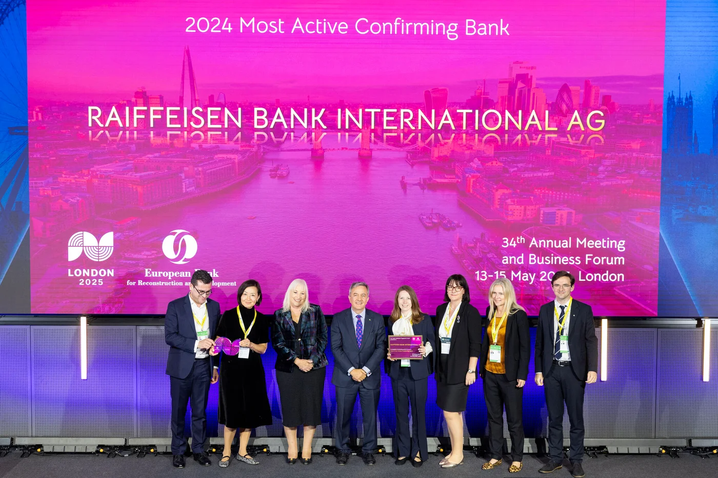 Eine Gruppe von Personen steht auf einer Bühne mit einer Auszeichnung vor einer großen Leinwand, die „2024 Most Active Confirming Bank Raiffeisen Bank International AG“ beim Business Forum in London zeigt.