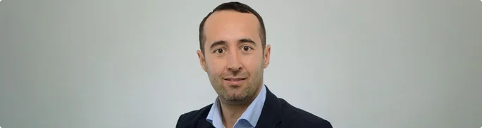 Portrait of Aliihsan Akgündüz in business attire with his face intentionally blurred for anonymity. Aliihsan is wearing a dark blazer over a light-colored shirt. The subject is posed against a plain, light gray background. The overall composition is simple and professional, suitable for corporate or privacy-related themes.
