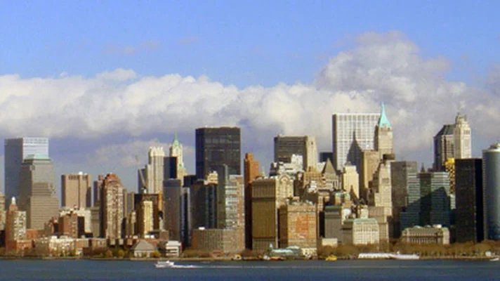 Panoramablick auf eine lebendige Stadtsilhouette mit einer Mischung aus modernen und historischen Gebäuden vor blauem Himmel mit weißen Wolken.
