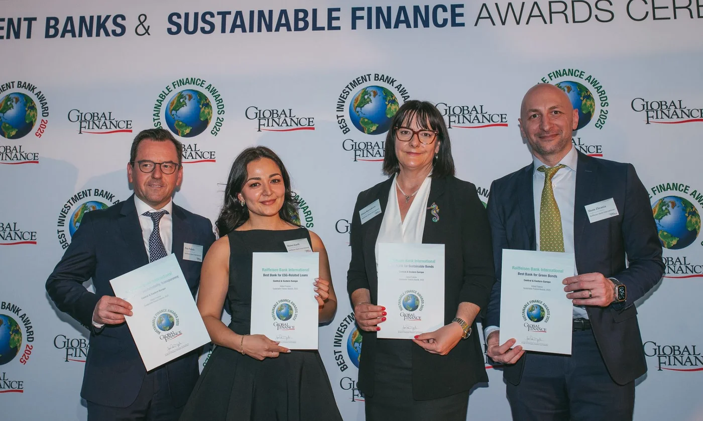 Vier Personen in formeller Kleidung halten Zertifikate vor einer Sustainable Finance Awards Fotowand.