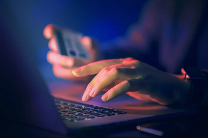 Dieses Bild zeigt eine Nahaufnahme einer Person, die ein Smartphone verwendet und gleichzeitig mit einem Laptop interagiert. Dies symbolisiert den Komfort von Mobile Banking und Online-Transaktionen in der heutigen digitalen Finanzlandschaft.