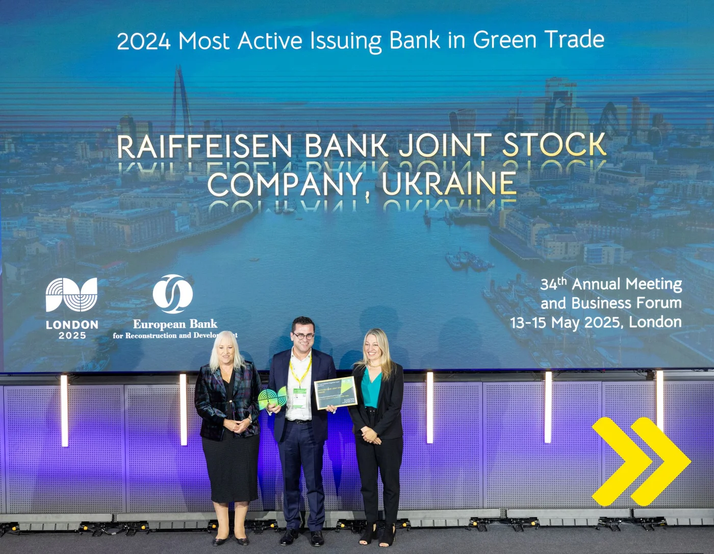Drei Personen stehen auf einer Bühne mit einer Auszeichnung vor einer großen Leinwand, die Raiffeisen Bank Joint Stock Company, Ukraine als „2024 Most Active Issuing Bank in Green Trade“ beim Business Forum in London auszeichnet.
