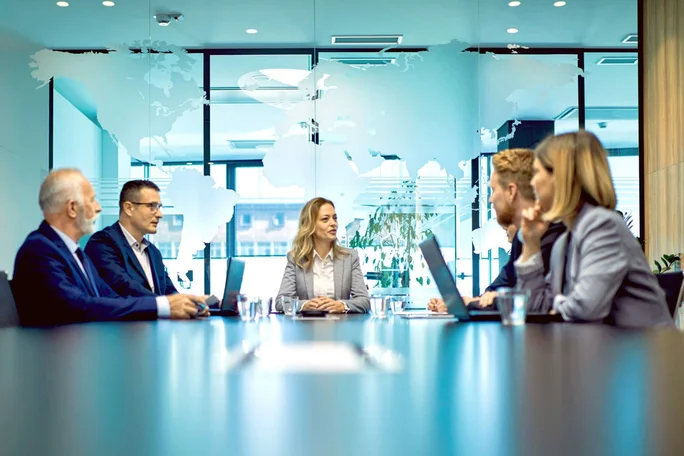 Geschäftsleute nahmen an einem strategischen Meeting an einem Konferenztisch in einem modernen Büro teil, an dessen Glaswand eine Weltkarte hing, die internationale Zusammenarbeit und Unternehmensführung symbolisierte.