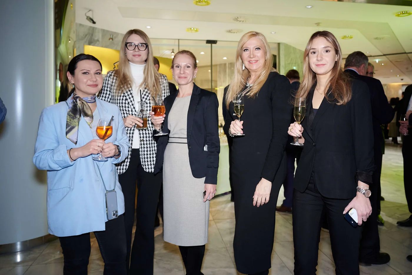 Eine Gruppe von Frauen in Businesskleidung steht gemeinsam bei einer Firmenveranstaltung und hält jeweils ein Glas Wein oder Cocktail.