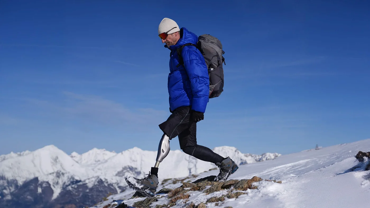 Ein inspirierendes Bild einer Person, die mit einer Prothese durch verschneite Berge wandert, verkörpert Entschlossenheit, Abenteuerlust und den Geist, Herausforderungen zu meistern.