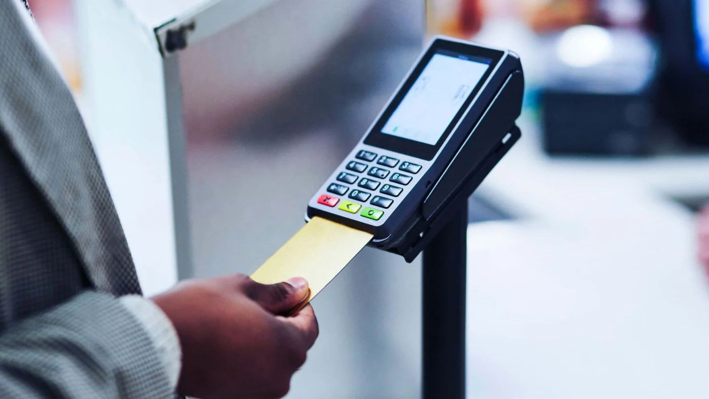 A customer holding a credit card while checking out at a cash register.