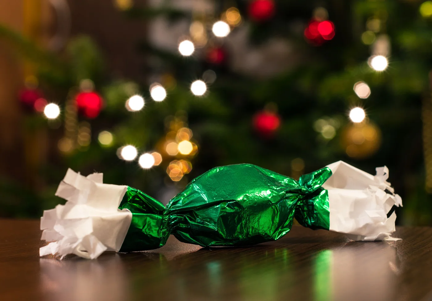 One green Hungarian Christmas candy (szaloncukor) in front of a Christmas tree.