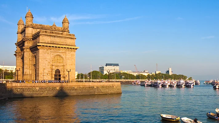 Atemberaubender Blick auf das Gateway of India, ein historisches Monument, das majestätisch am Wasser steht, mit Booten in der Nähe und klarem, blauem Himmel darüber.