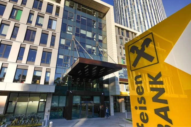 Der Eingang der Raiffeisen Bank Rumänien mit moderner Architektur, großen Glasfronten und dem auffälligen gelben Banklogo im Vordergrund.