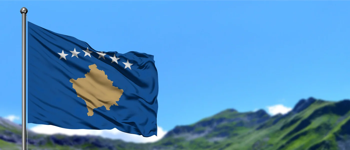 Kosovo flag waving in the blue sky with green fields at mountain peak background. Nature theme.