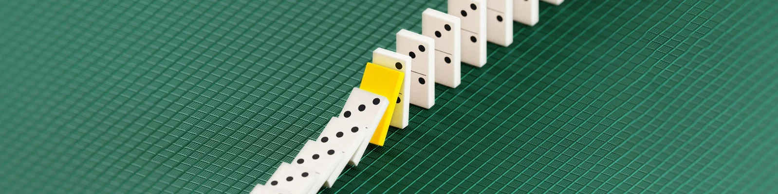 Eine Reihe weißer Dominosteine mit einem einzelnen gelben Dominostein auf einem grünen strukturierten Hintergrund, der die Wirkung von optimiertem Working Capital symbolisiert.