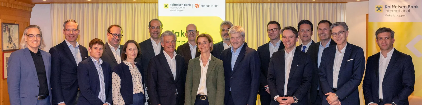 Eine Gruppe von Fachleuten versammelt sich bei einer Veranstaltung der Raiffeisen Bank International und steht vor gebrandeten Bannern und einem Vorhang-Hintergrund.