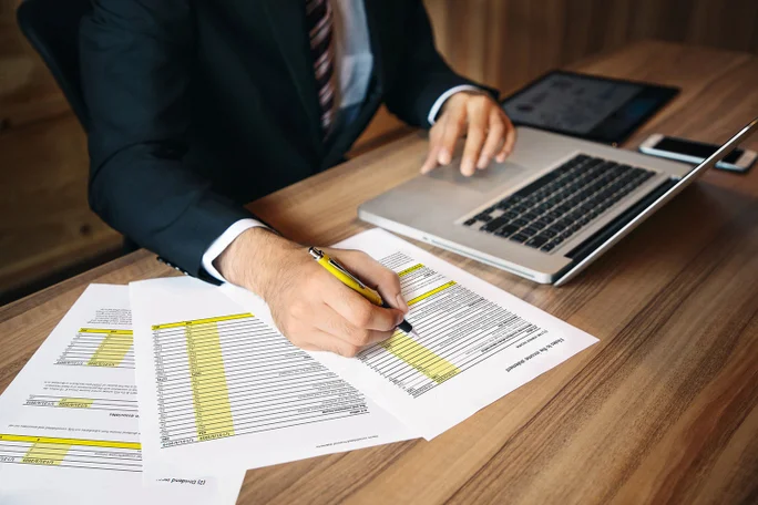 Ein Geschäftsmann im Anzug prüft sorgfältig Finanzdokumente und nutzt während einer umfassenden Finanzbewertung einen Laptop zur Datenanalyse.