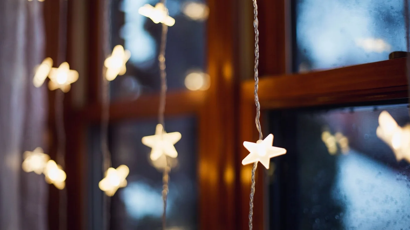 Leuchtende sternförmige Lichterketten hängen vor einem Fenster und sorgen für eine gemütliche und festliche Stimmung.