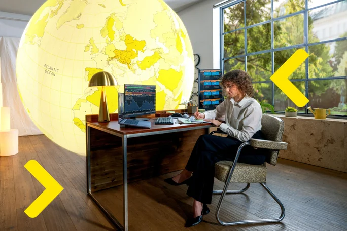 Woman sitting at a desk working, with a large globe map in the background, next to window with garden view