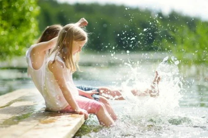 Zwei Kinder planschen mit den Füßen an einem See.