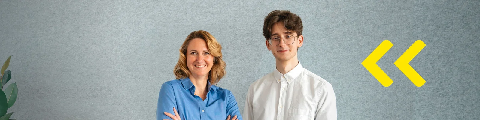 Two people stand side by side in front of a plain gray wall, with their faces blurred for anonymity. One person wears a blue shirt with folded arms, while the other wears a white button-up shirt. A pair of bright yellow chevron arrows appears on the right side of the image, adding a modern graphic element. The overall scene suggests a professional or corporate setting with a clean, minimal background.