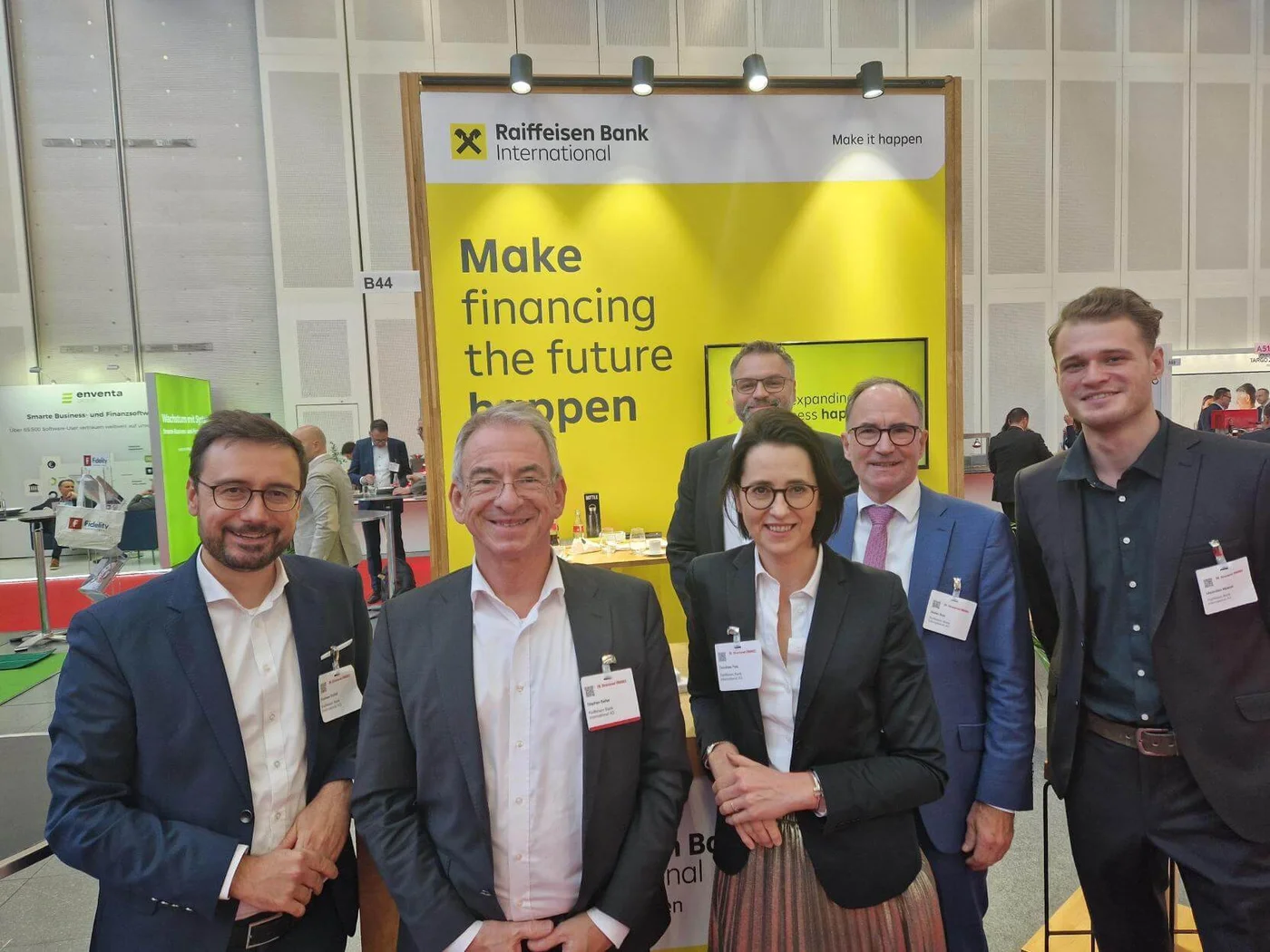 Teammitglieder der Raiffeisen Bank International an ihrem Messestand mit dem Slogan „Make financing the future happen“. Das professionelle Umfeld hebt das Engagement der Bank für Innovation und Kundenbindung bei Branchenevents hervor.