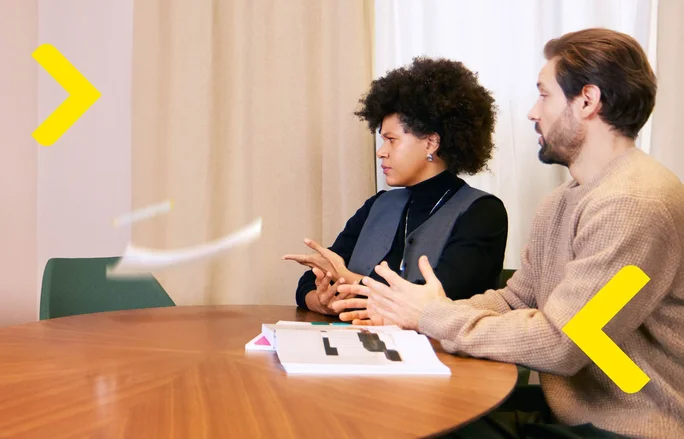 Zwei Fachleute sitzen an einem runden Tisch und diskutieren. Vor ihnen liegen Geschäftsdokumente und Berichte, was Teamarbeit und Zusammenarbeit in einem Unternehmensumfeld hervorhebt.