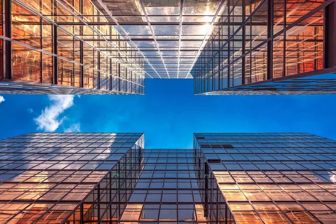 Blick nach oben auf moderne Wolkenkratzer aus Glas, die Sonnenlicht und blauen Himmel reflektieren und urbane Architektur, modernes Design und städtische Innovation präsentieren.
