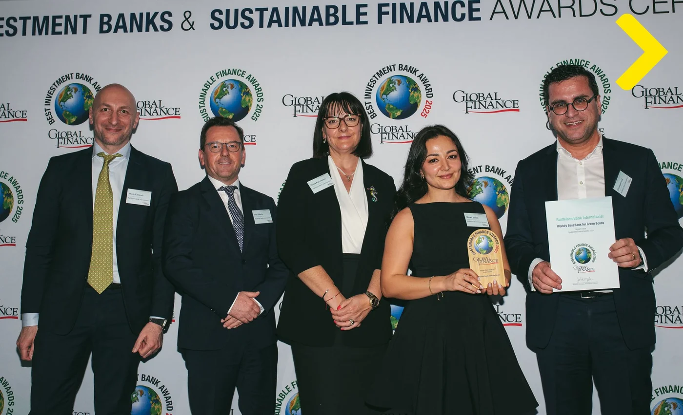 Eine Gruppe von Personen in formeller Kleidung steht bei einer Preisverleihung mit einer Trophäe und einer Urkunde vor einer Sustainable Finance Awards Fotowand.