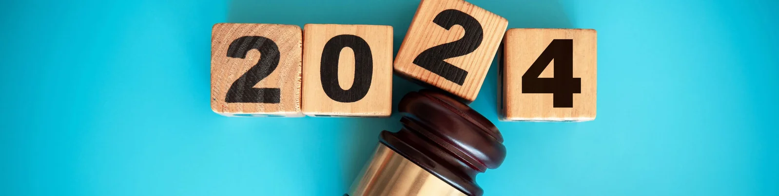 Holzwürfel, die das Jahr "2024" anzeigen, neben einem Hammer, vor einem hellen türkisfarbenen Hintergrund, der für Neuanfänge und Vorsätze steht.