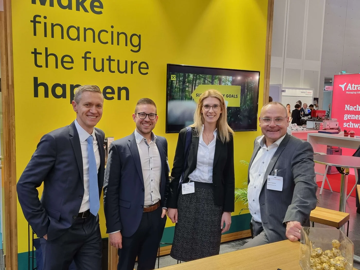 Vertreter:innen der Raiffeisen Bank International stehen an ihrem Messestand mit dem Slogan „Make financing the future happen“. Das professionelle Umfeld unterstreicht den Fokus der Bank auf nachhaltige Ziele und Branchenengagement.