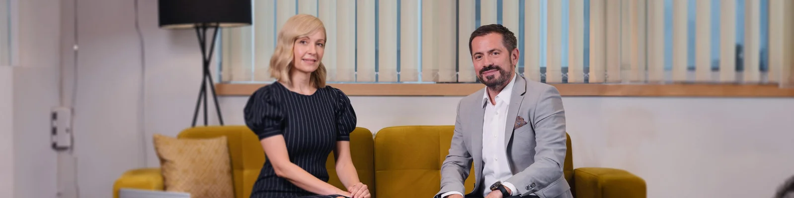 A professional businesswoman and businessman seated on a yellow couch in a modern office, engaged in a formal conversation, symbolizing collaboration and leadership