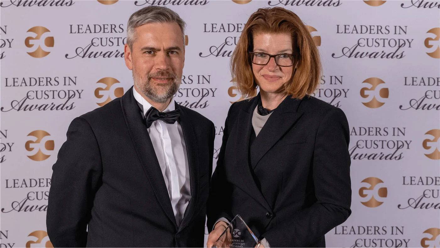 Two individuals dressed in formal attire pose at the Leaders in Custody Awards. The backdrop features the event's logo and name, highlighting a prestigious occasion.