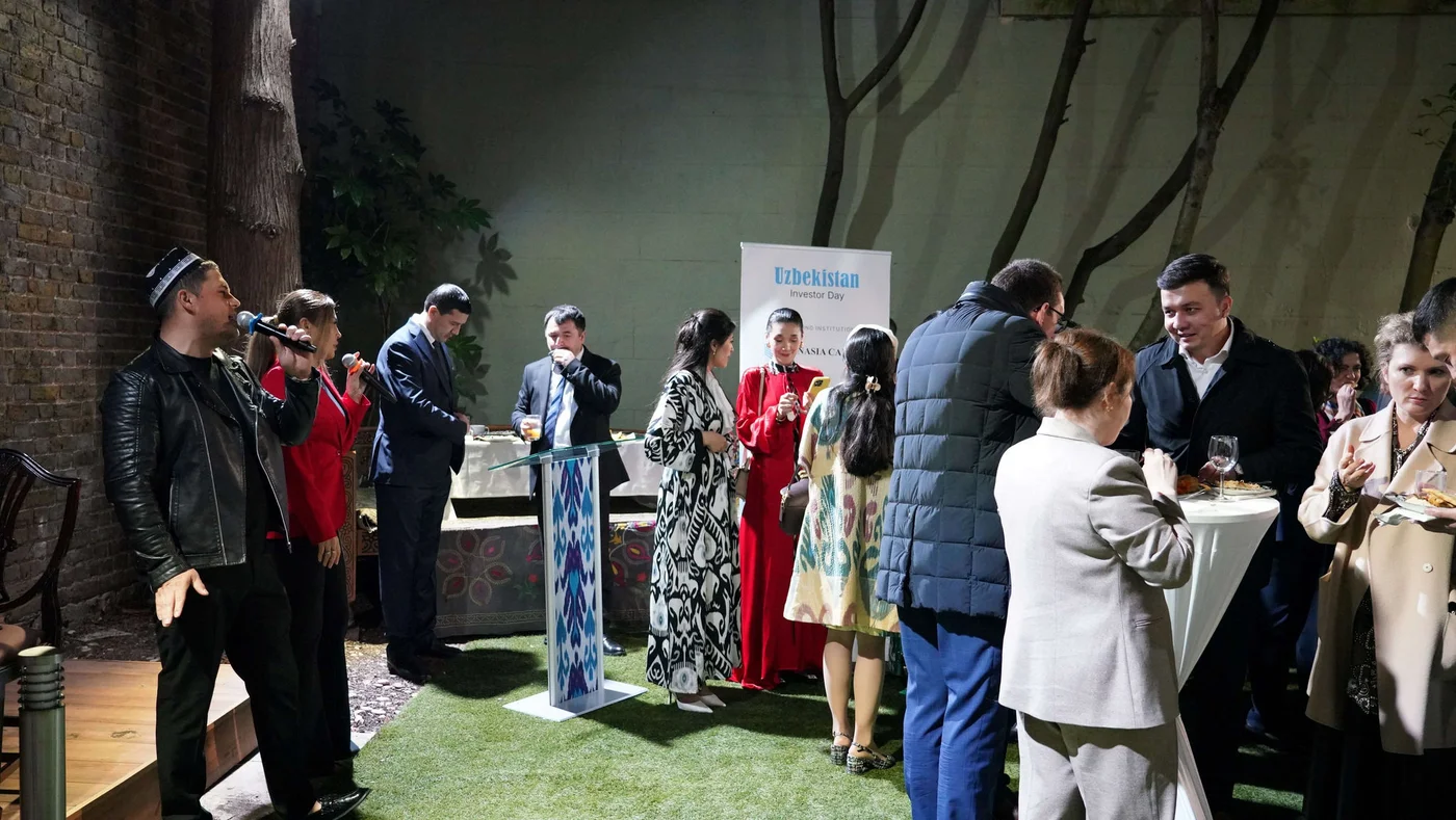 Guests at the Uzbekistan Investor Day event, mingling and enjoying refreshments outdoors, with performers on stage and informational banners in the background