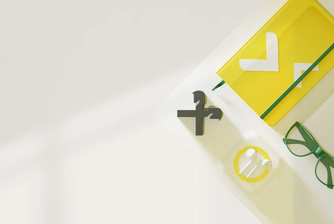 Ein ordentlich arrangierter Arbeitsplatz mit gelbem Notizbuch, grüner Brille, kabellosen Ohrhörern im Ladecase und einem dekorativen Symbol. Das Setup ist minimalistisch und gut beleuchtet – ideal für produktives Arbeiten.