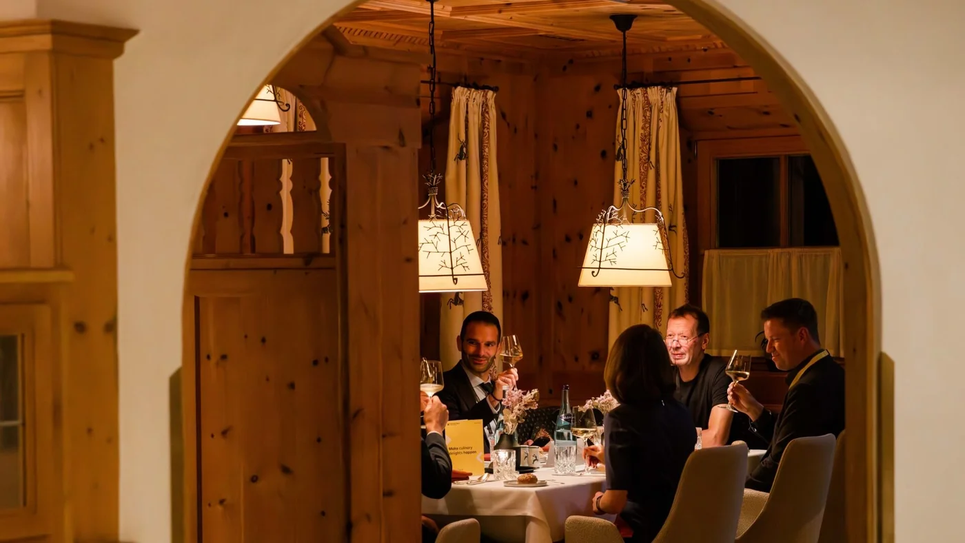 Eine Gruppe von Menschen sitzt um einen Tisch herum und genießt Abendessen und Getränke in einem warmen, holzgetäfelten Restaurant mit Hängelampen und Vorhängen.
