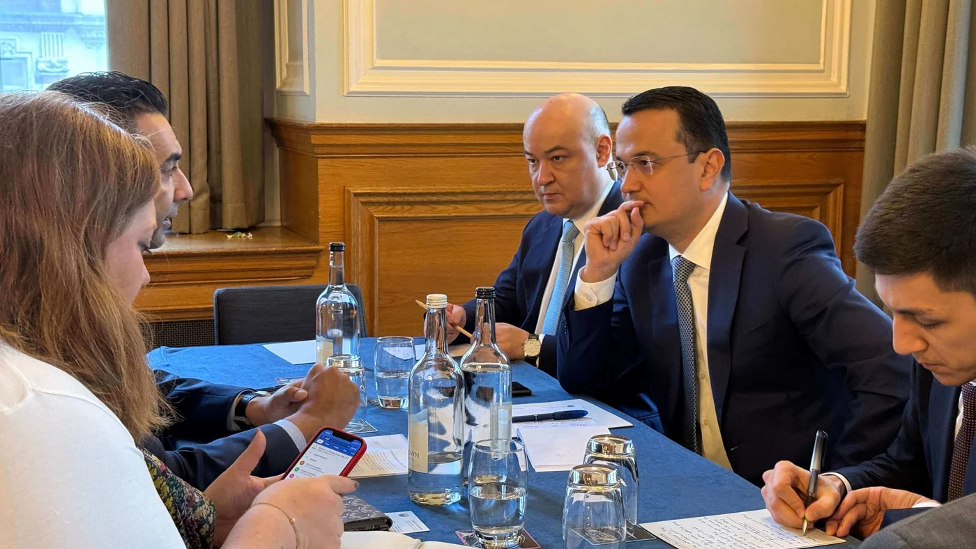 Individuals engaged in a detailed business discussion around a table, with documents, smartphones, and bottles of water present, in a formal setting