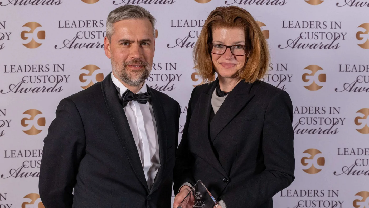 Two people in formal attire stand together holding an award in front of a Leaders in Custody Awards backdrop.