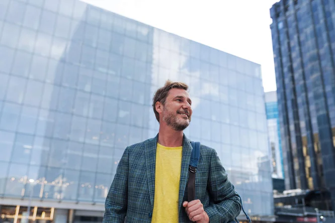 Eine Person in stilvoller Kleidung steht selbstbewusst in einem geschäftigen Geschäftsviertel, umgeben von modernen Wolkenkratzern und reflektierenden Glasgebäuden.