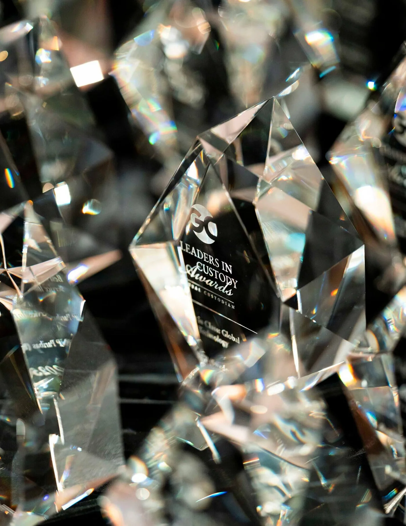 A close-up of a faceted crystal award with engraved text, reflecting light and surrounded by other crystals.