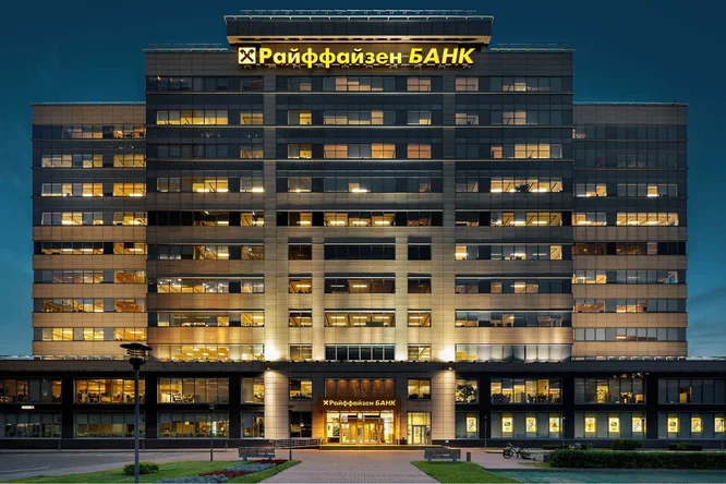 Nachtansicht des Raiffeisen Bank Russland Gebäudes mit beleuchteten Fenstern und Beschilderung – moderne Architektur vor dunklem Himmel.