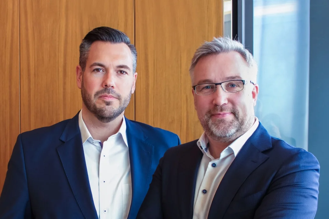 Zwei professionelle Männer in Geschäftskleidung, die vor einem Holz-Hintergrund stehen und Führung im Unternehmensberatung darstellen.