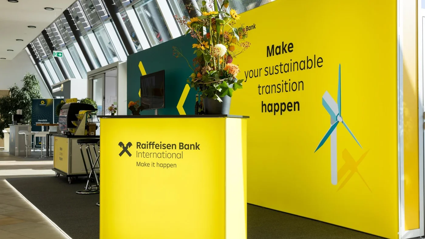 Ein leuchtend gelber Stand der Raiffeisen Bank mit Blumen und Werbematerialien in einem Innenbereich.