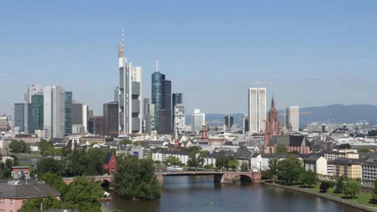 Panoramablick auf die Skyline von Frankfurt mit modernen Wolkenkratzern und historischen Gebäuden, durch die die Main fließt – unter klarem, blauem Himmel.