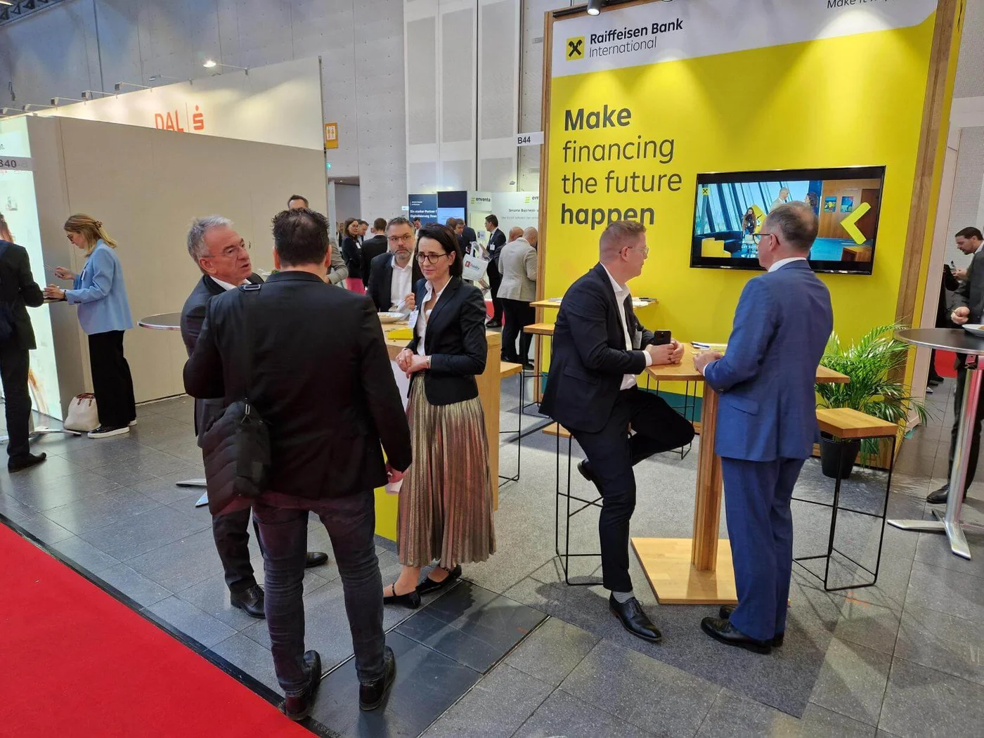 Messestand der Raiffeisen Bank International auf einer Fachmesse mit dem Slogan „Make financing the future happen“. Besucher:innen führen Gespräche und vernetzen sich – dies unterstreicht die interaktive und professionelle Atmosphäre der Veranstaltung.