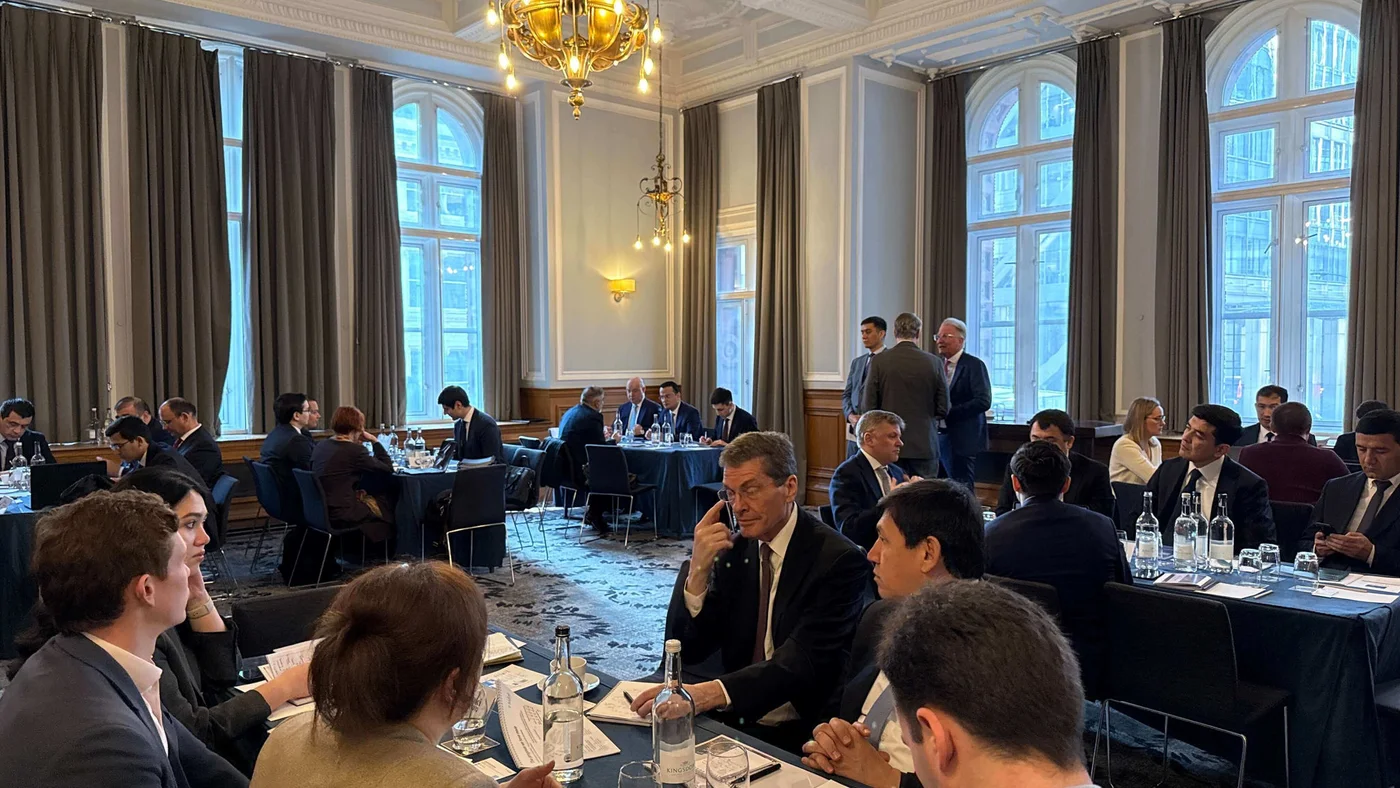 A large group of professionals attending a corporate conference, seated at tables in a grand room with high ceilings, chandeliers, and tall windows.