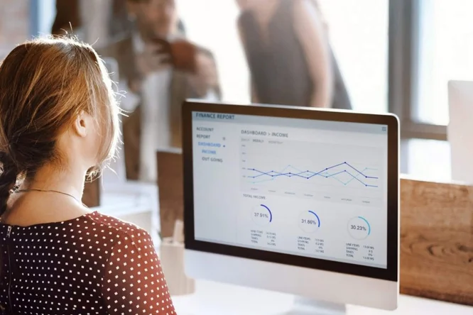 Eine Frau betrachtet einen Finanzbericht mit Diagrammen und Grafiken auf einem Desktop-Computer in einem modernen Büro.