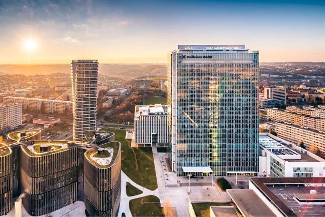 Luftaufnahme der Raiffeisen Bank Tschechien Zentrale und umliegender moderner Gebäude bei Sonnenuntergang. Die Stadtlandschaft und Architektur werden vom warmen Licht der untergehenden Sonne beleuchtet.