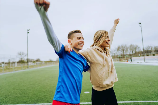 Two individuals expressing joy and triumph on a sports field, capturing the spirit of teamwork and achievement in an outdoor setting.