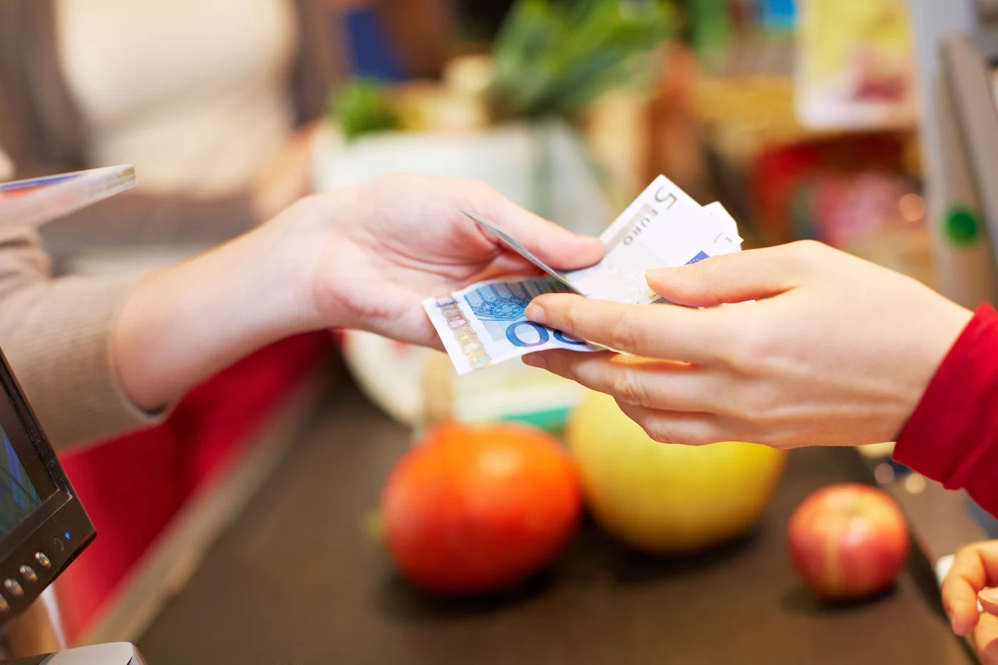 Hände übergeben zwei Euroscheine an der Kasse im Supermarkt