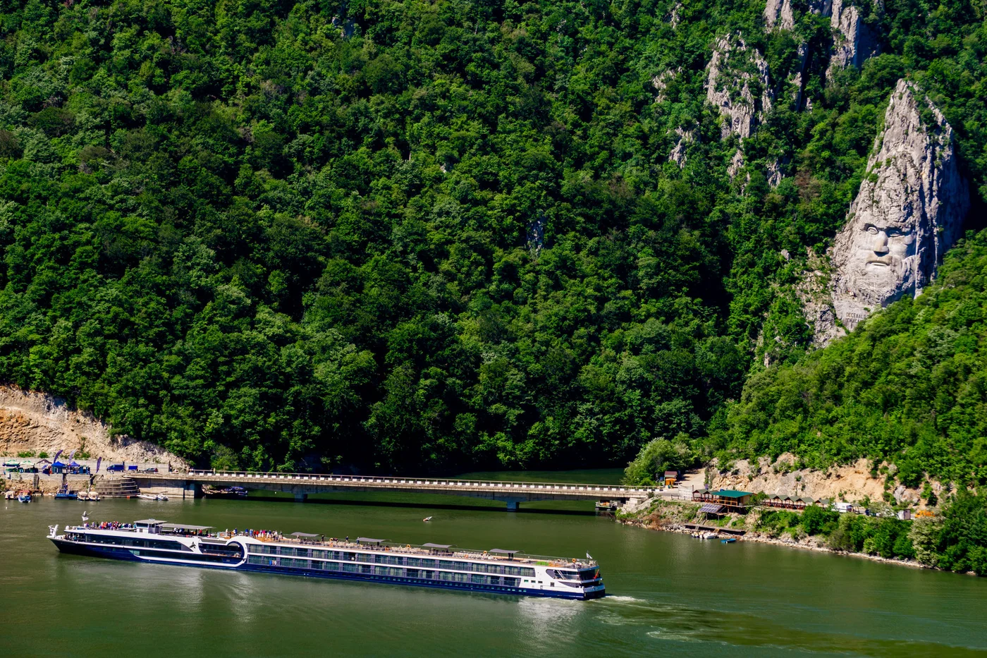 DUBOVA, ROMANIA - MAY 8, 2018: Cruise ship passing by rock sculpture of Decebalus in Danube gorge, near Dubova, Romania. Sculpture of Decebalus, the last king of Dacia, was made in 1994.