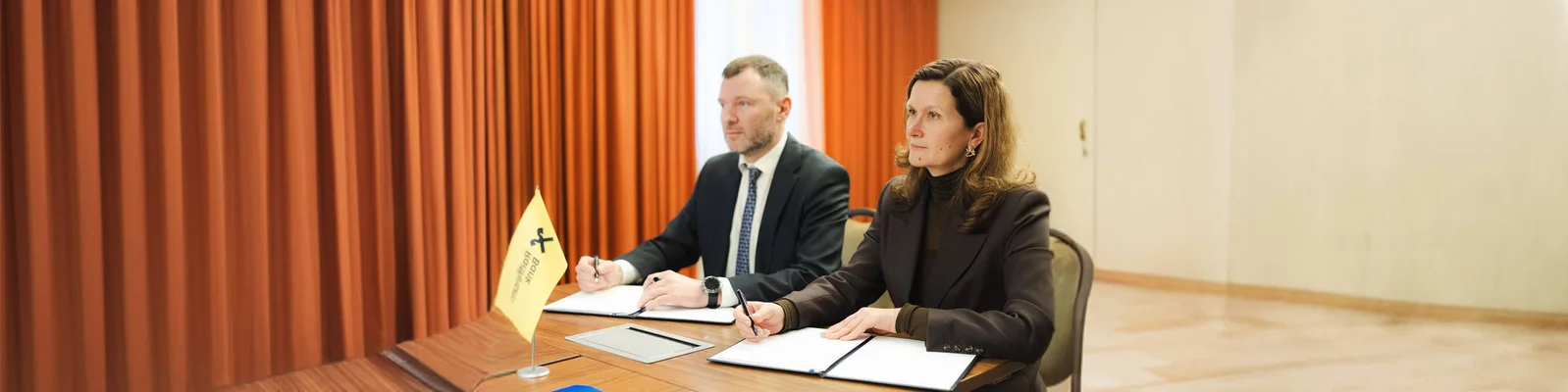 Zwei Erwachsene sitzen an einem Tisch und führen ein formelles Geschäftstreffen. Sie schreiben auf Dokumenten; auf dem Tisch liegt eine gelbe Fahne mit der Aufschrift „Höflichkeitspunkt“. Orangefarbene Vorhänge und neutrale Farbtöne sowie Businesskleidung verleihen dem Raum eine professionelle Atmosphäre. Das Bild vermittelt einen seriösen und kooperativen Eindruck.
